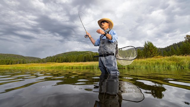 Angler fishing in a lake with a mountain in the background.