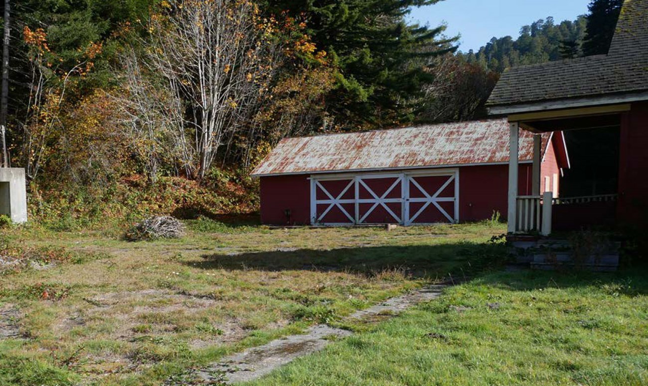 A garage and house with a porch face a flat, open area with a paved walkway